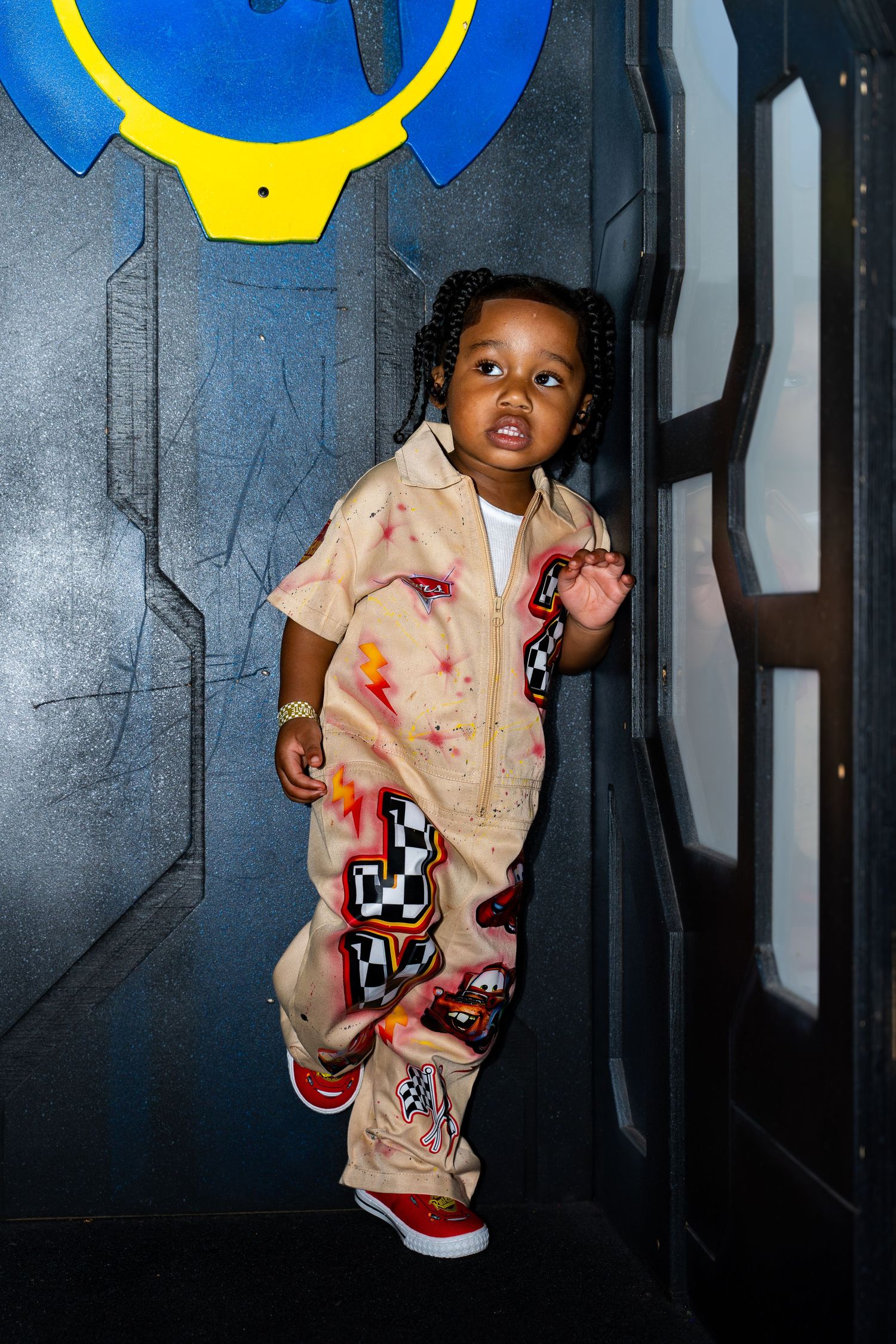 Toddler in colorful painted jumpsuit stands confidently in front of a sci-fi themed backdrop.