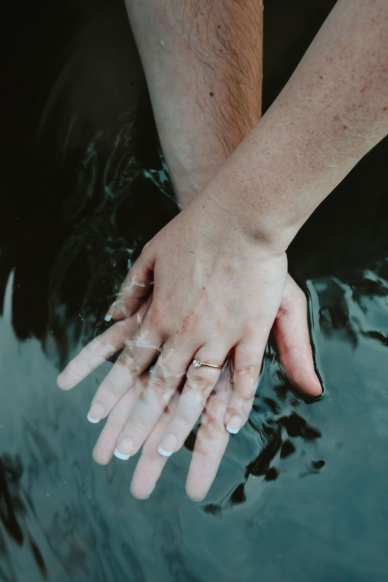 Two hands touching over water, one wearing a gold engagement ring, symbolizing love and commitment.