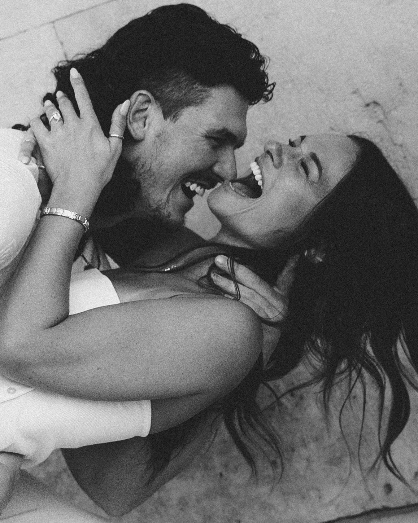 Black and white photo of a happy couple laughing and embracing, with the woman's long hair flowing as they share a joyful moment.