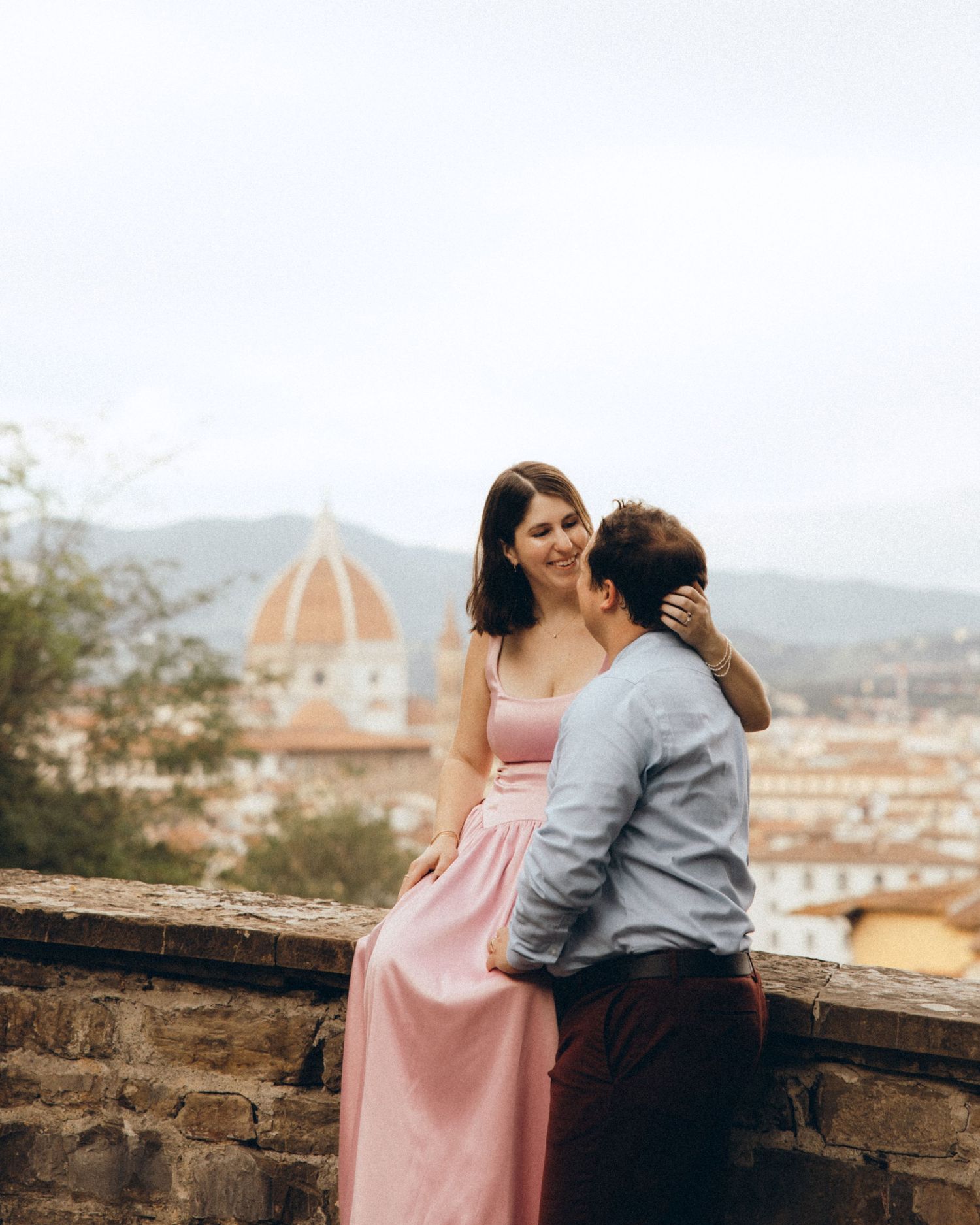 Romantic couple embracing on a stone terrace overlooking Florence, with the Duomo and rolling hills in the background.