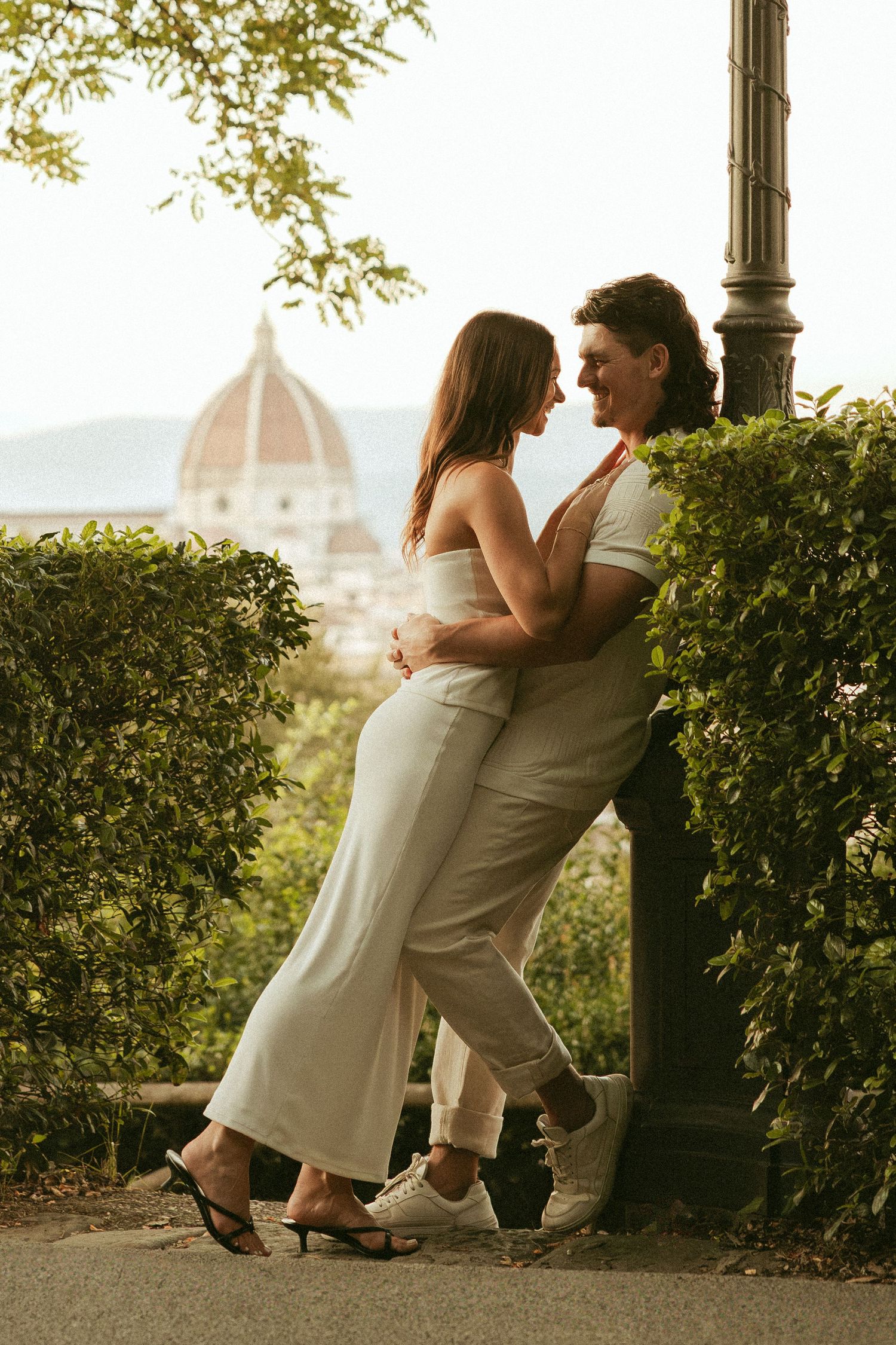 Couple in white outfits embracing against a lamppost with a view of Florence's Duomo dome in the background.