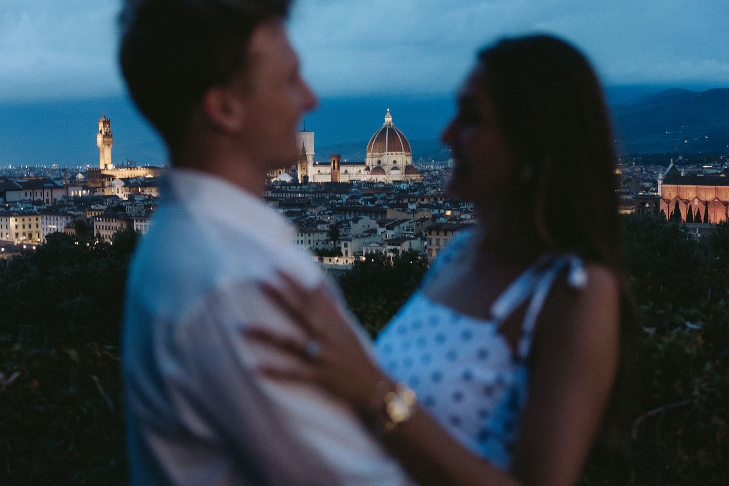 Romantic couple embracing at dusk with the illuminated Florence skyline and Duomo cathedral softly blurred in the background.