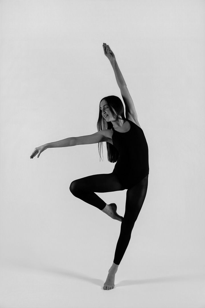 Black and white photo of a female dancer balancing on one foot with arms extended in a modern dance pose.
