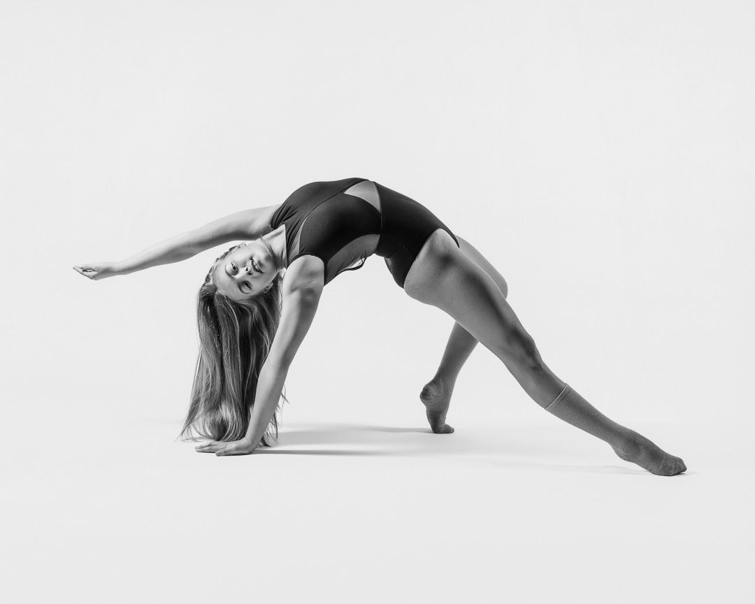 Graceful dancer in black leotard performs contemporary dance pose against white background in monochrome.