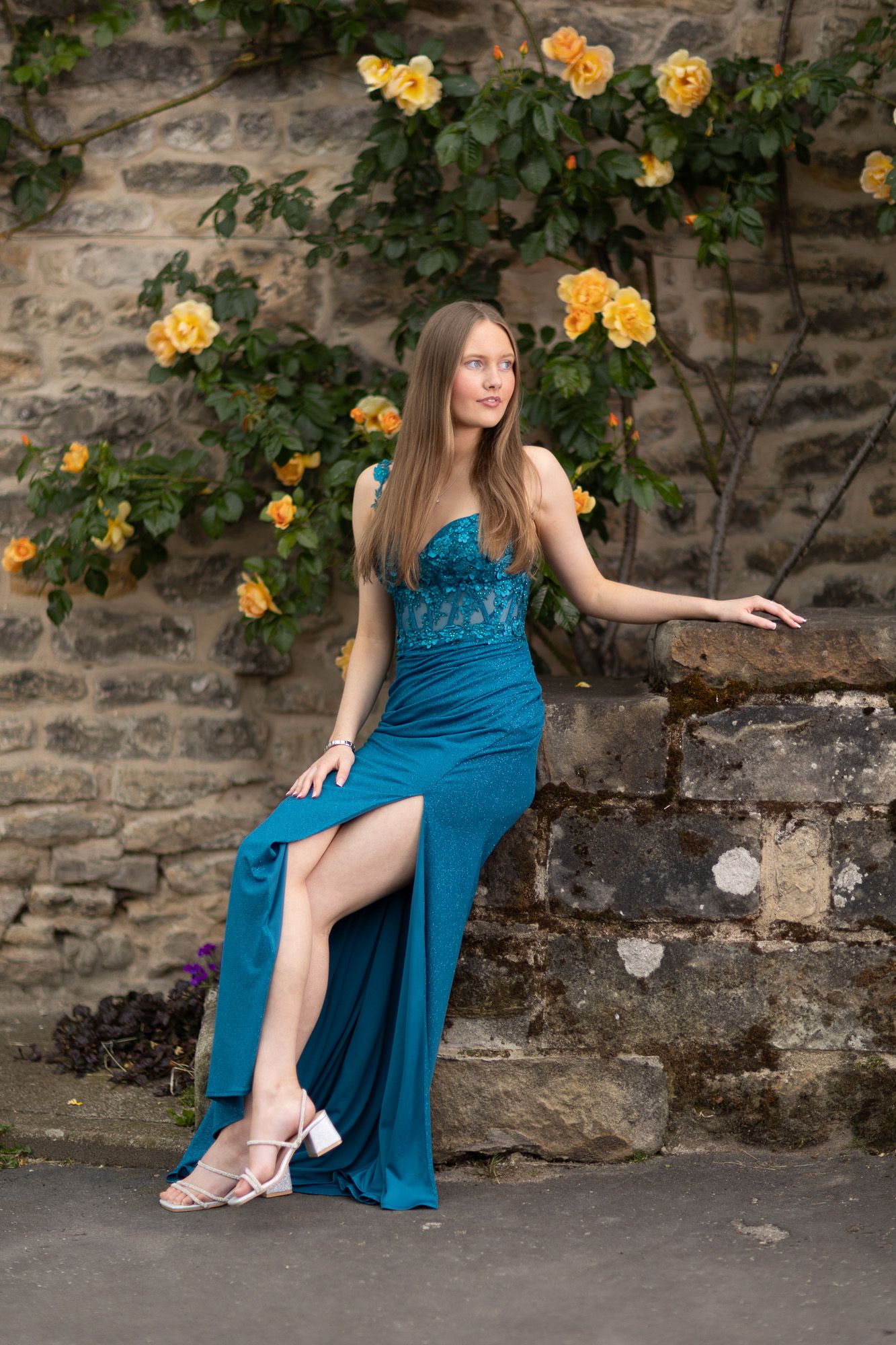 Elegant blue dress photographed against stone wall with blooming yellow roses.