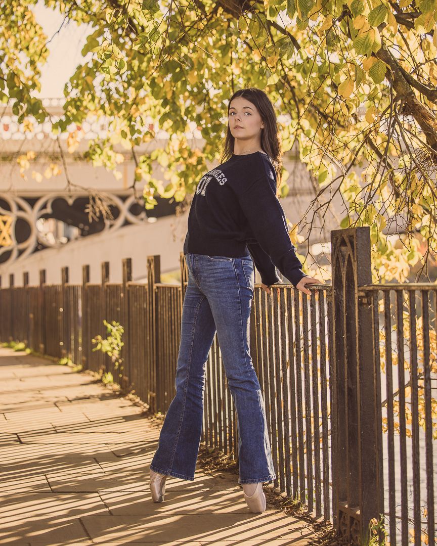 Casual autumn portrait against yellow leaves and iron fence in warm sunlight.