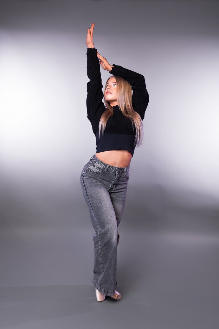 Modern dancer in crop top and jeans performs against grey backdrop.