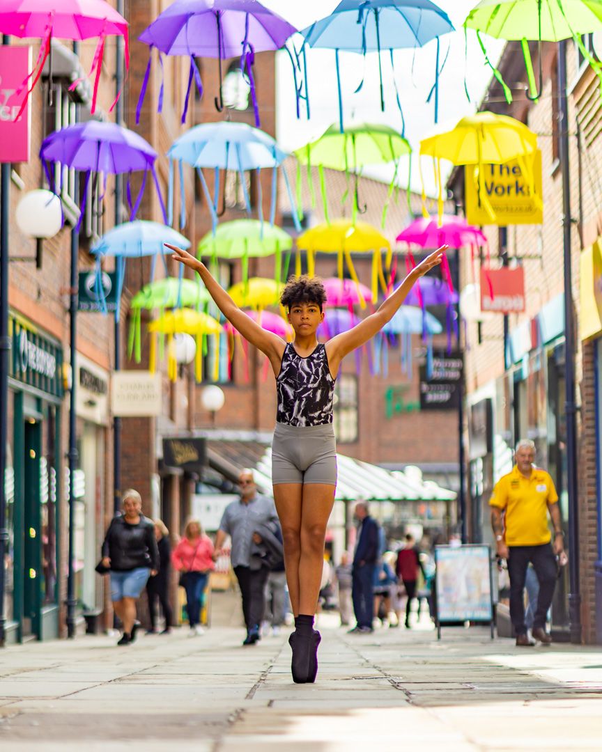 Colorful umbrellas hanging over city street with dancers performing underneath.