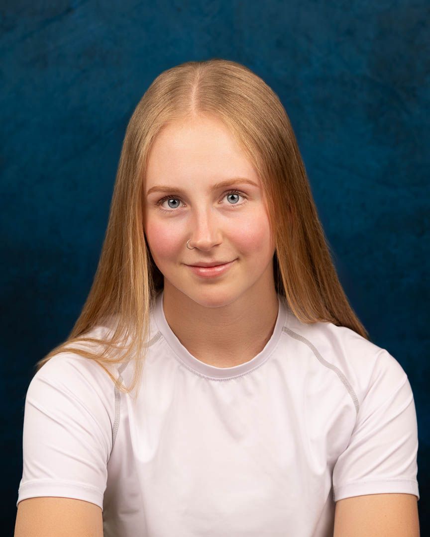 Young blonde girl with blue eyes smiling in white t-shirt against dark blue studio background.