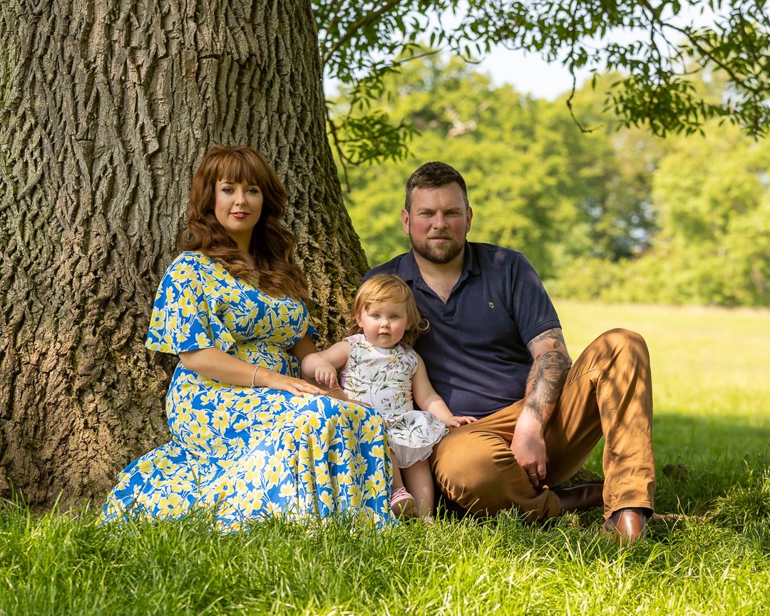 A series of outdoor family photos taken under a large tree in a sunny meadow.