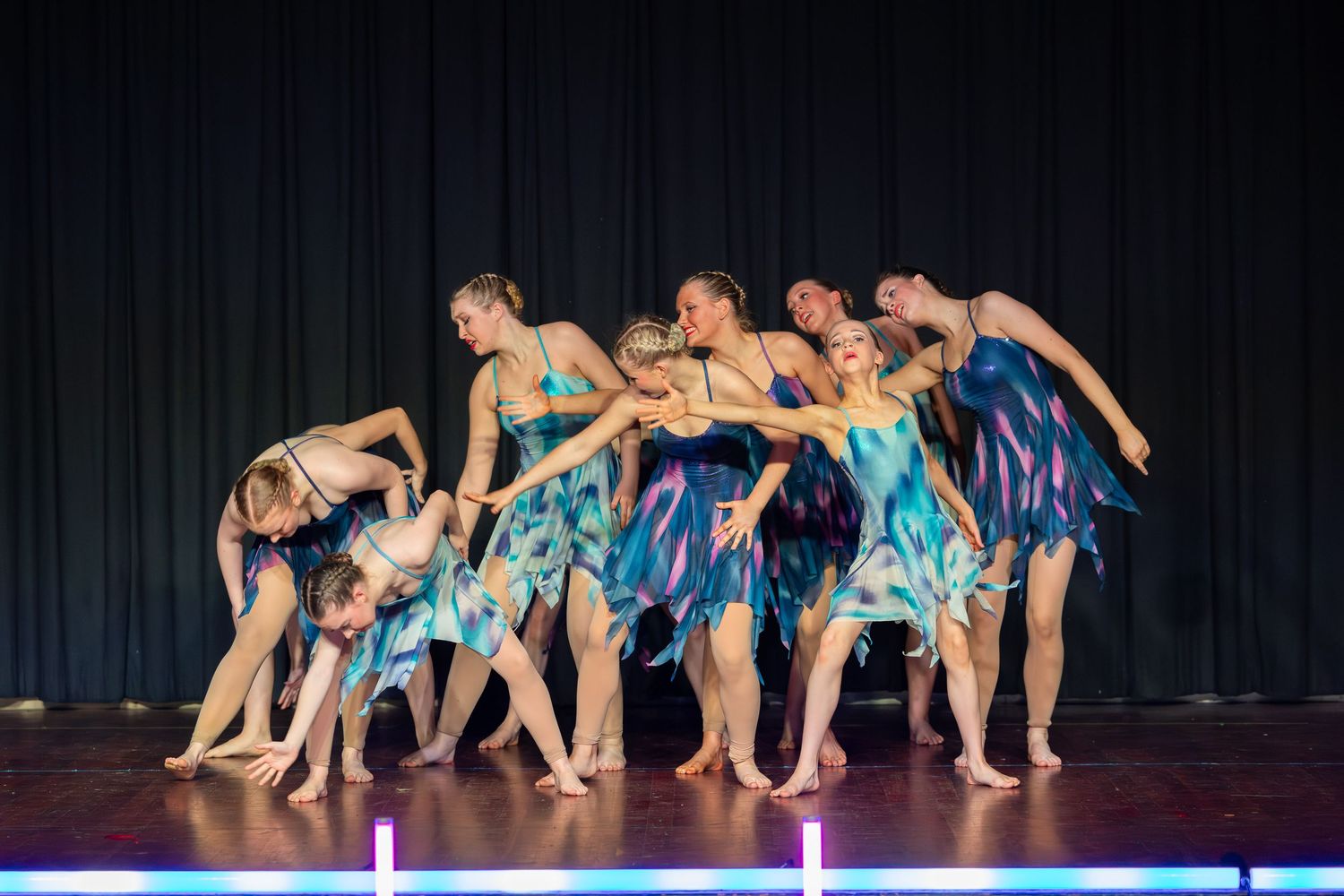 Group of dancers in blue floral costumes performing a contemporary dance routine on a stage.