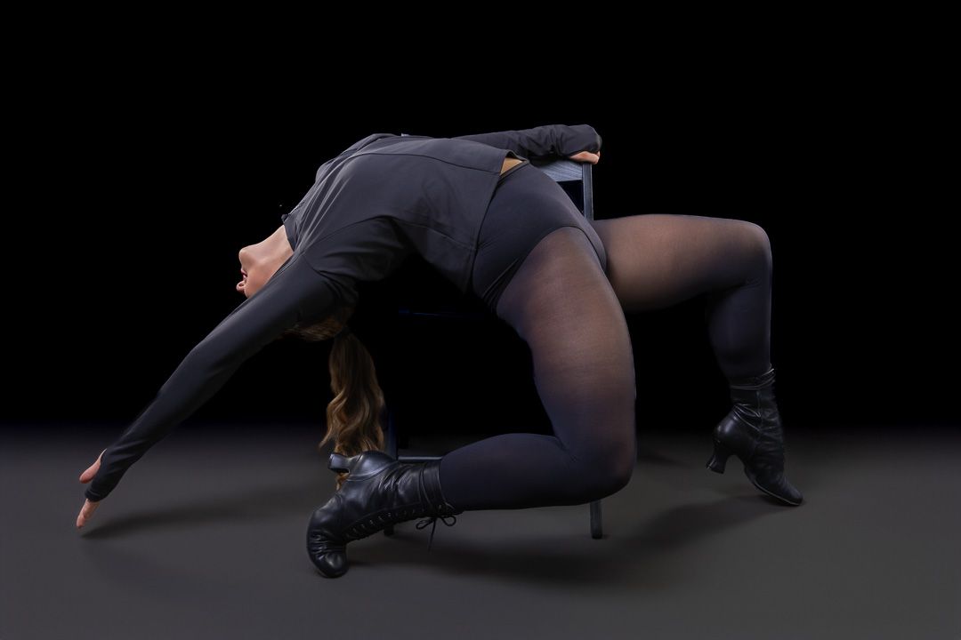 Contemporary dancer performs floor choreography in dark attire.