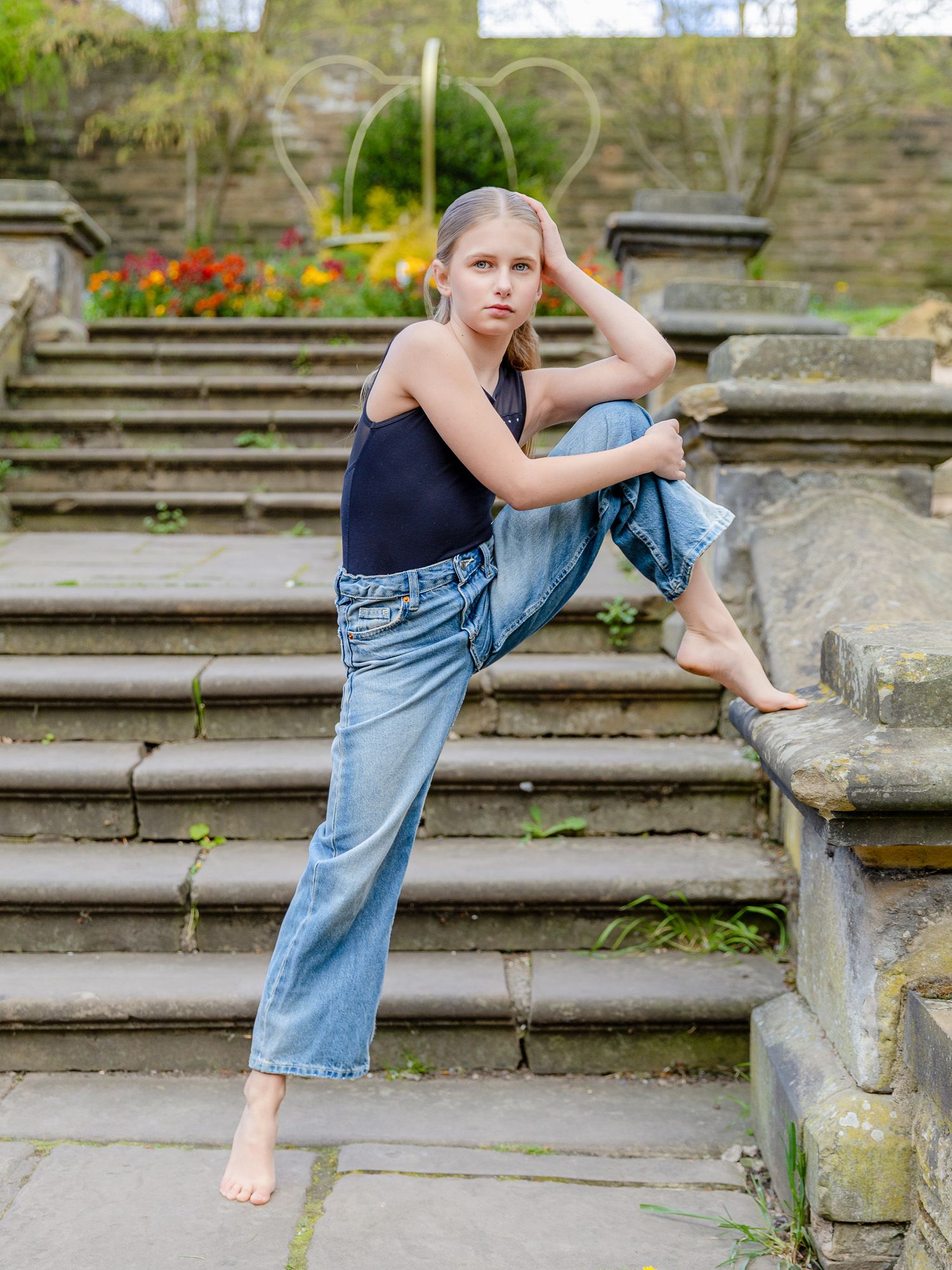 Young girl in jeans and black top posing on stone steps in a garden setting.
