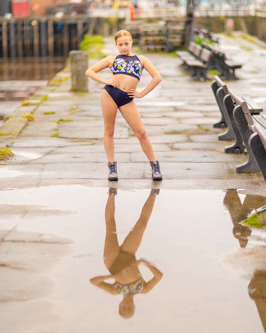 Dancer strikes dynamic poses reflected in puddles on wet stone pavement.