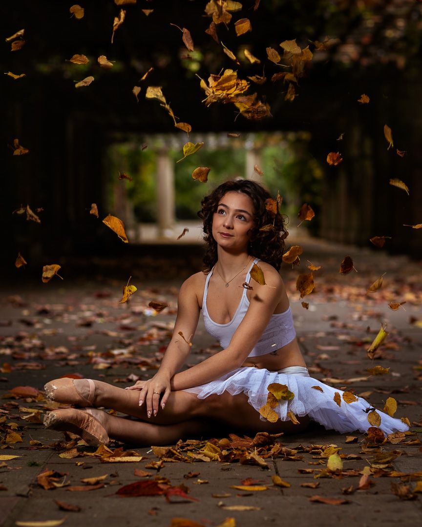 Dancer reclining among scattered autumn leaves in an artistic outdoor portrait session.