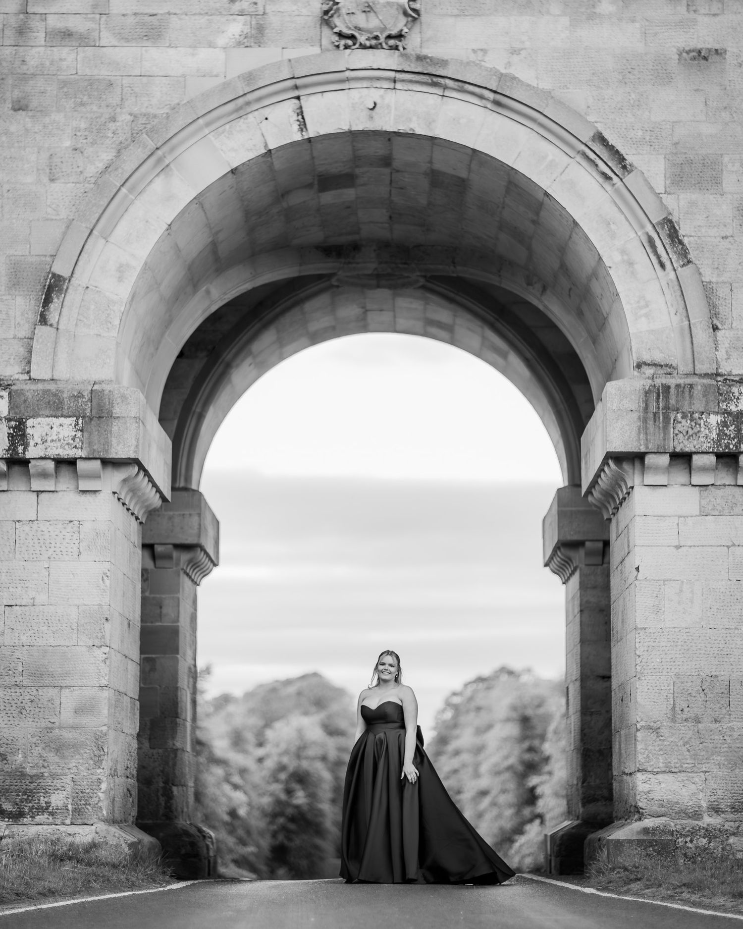 A dramatic black and white photo under a stone archway featuring a flowing black gown.