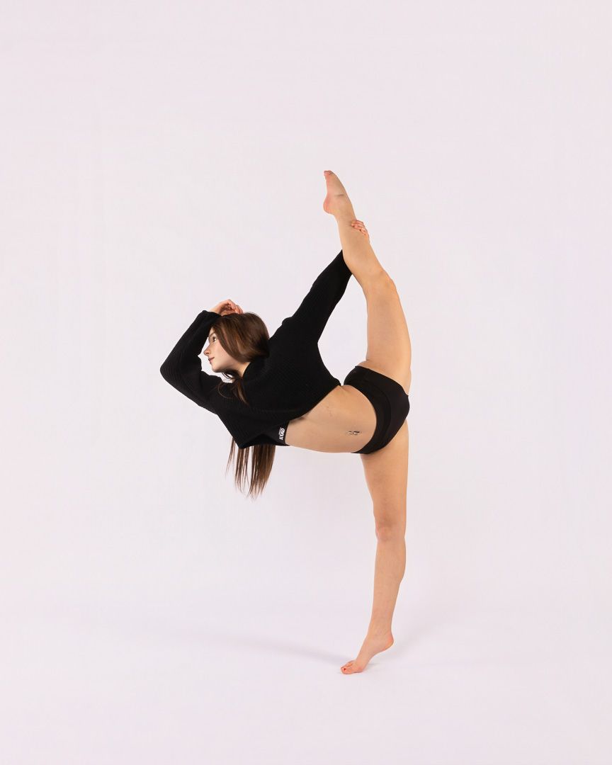 Dancer in black athletic wear performs a graceful high kick against a white studio background.