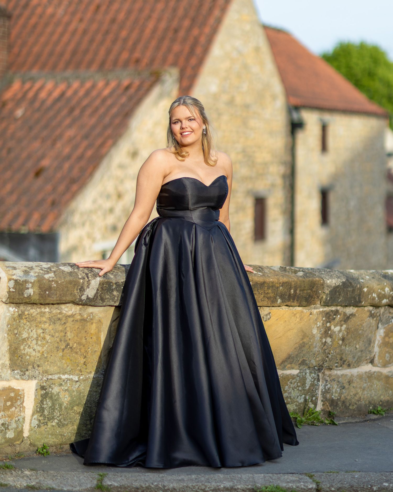 A woman in a black formal gown poses against a rustic stone wall backdrop in a series of elegant shots.