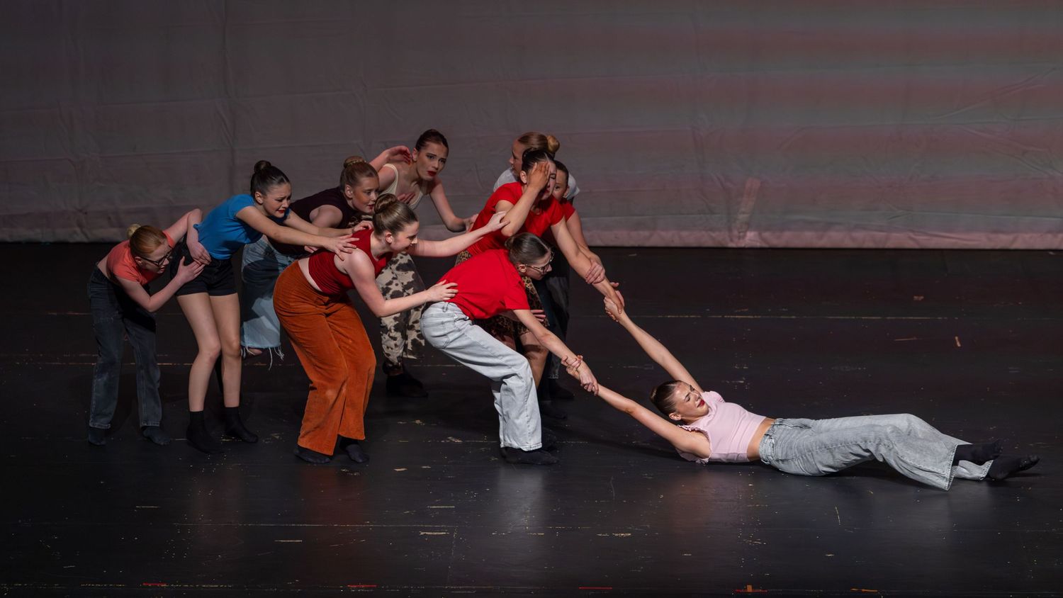 Group of dancers performing a dramatic contemporary dance routine on a dark stage under bright spotlights.