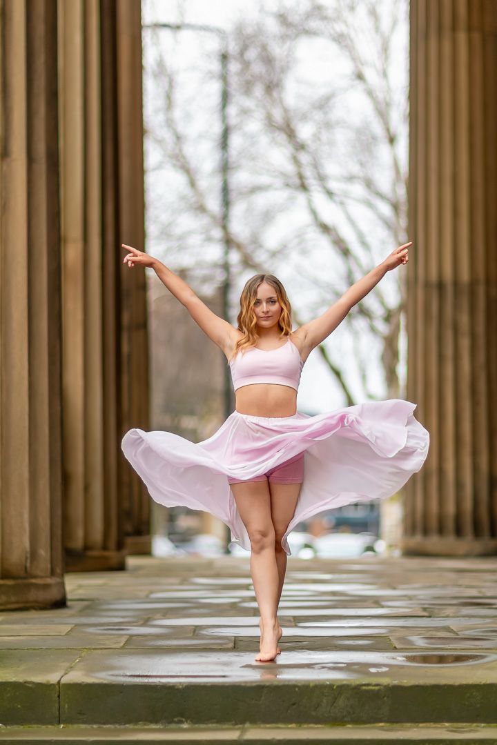 Graceful dance movements captured in pink outfit against classical stone column backdrop.