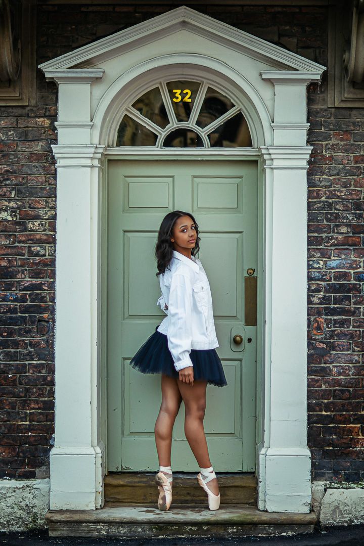 Dancer poses in ballet shoes by elegant green Georgian door with white columns.