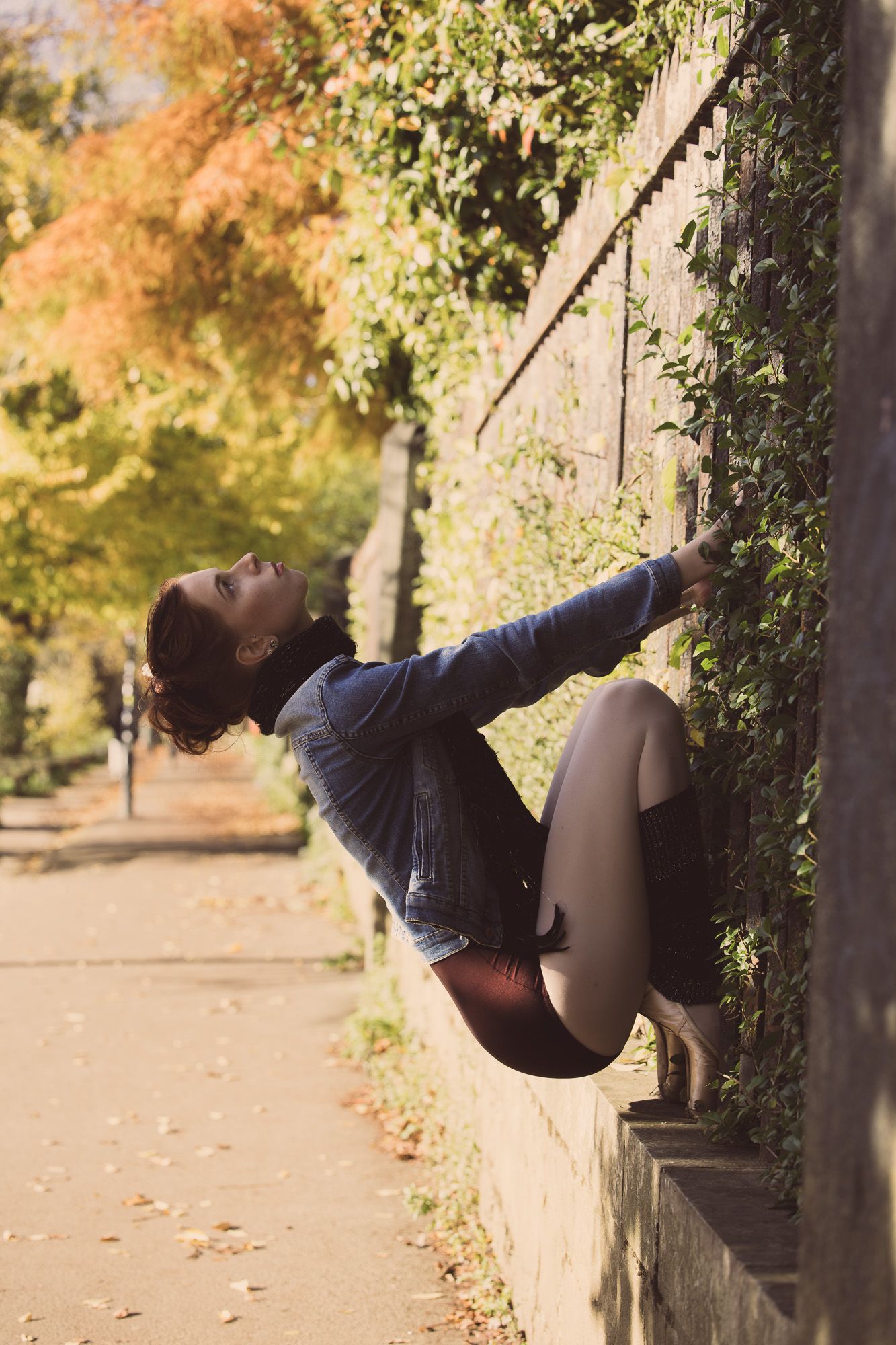 A figure in black clothing performs a graceful swing sequence on a low wall during autumn.