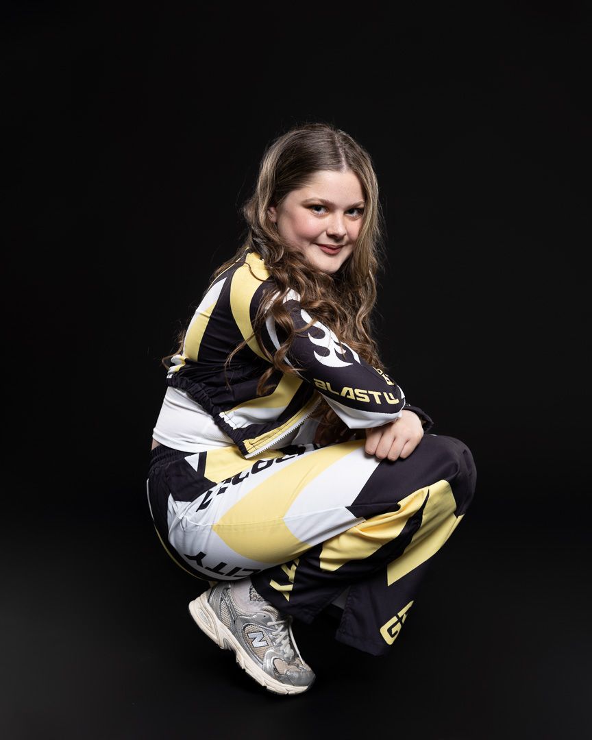 Young girl crouching in black and yellow racing suit against dark background.