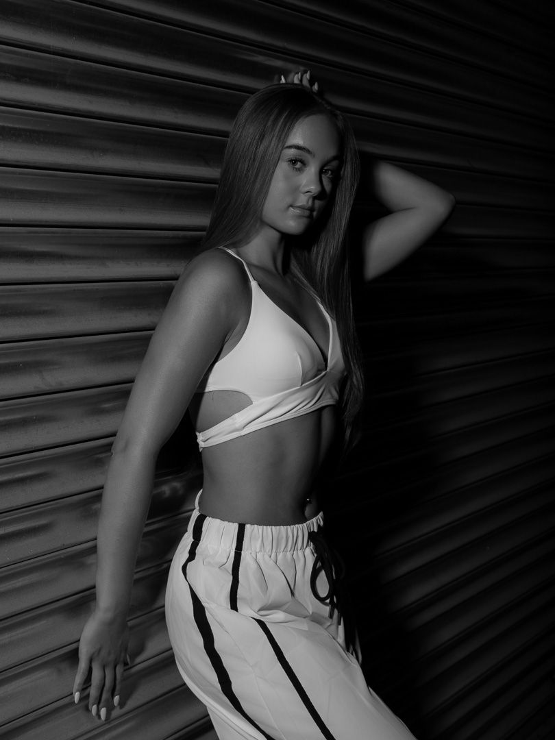 Black and white photo of a woman in a crop top and striped pants posing confidently against a metal shutter backdrop.