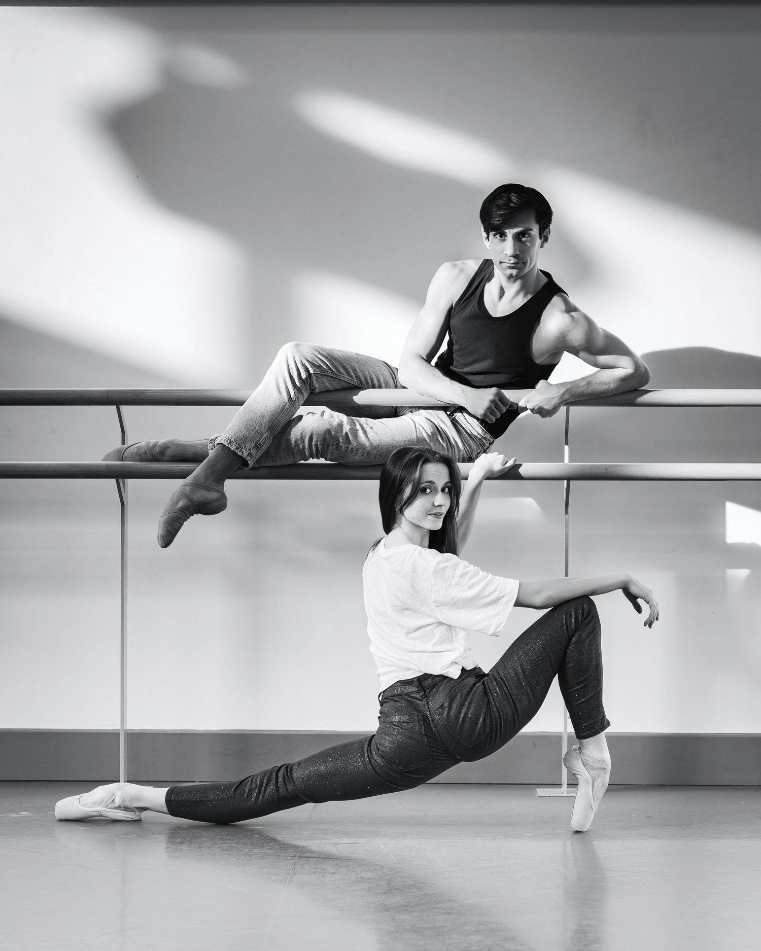 A dancer performs a graceful floor sequence in a modern dance studio with a ballet barre and natural lighting.