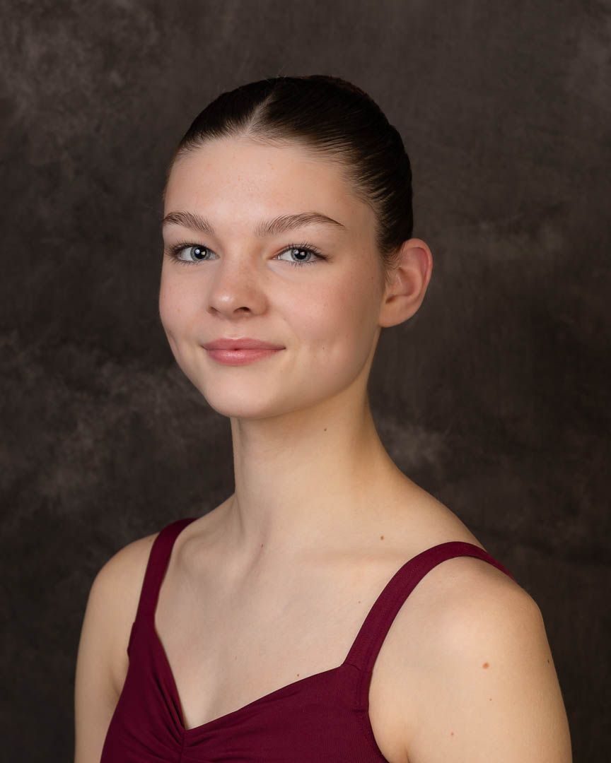 Young female ballet dancer in burgundy leotard with sleek updo hairstyle poses for professional portrait.