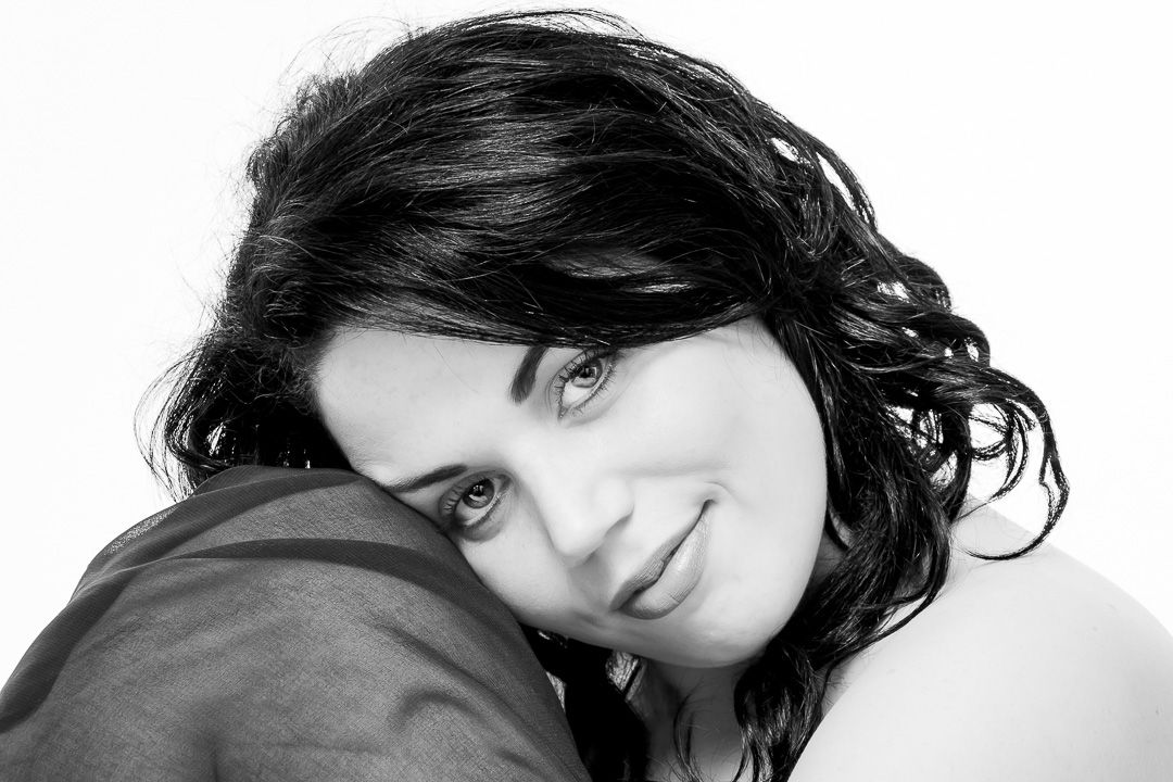 Black and white portrait of a person with dark curly hair resting against a dark surface.