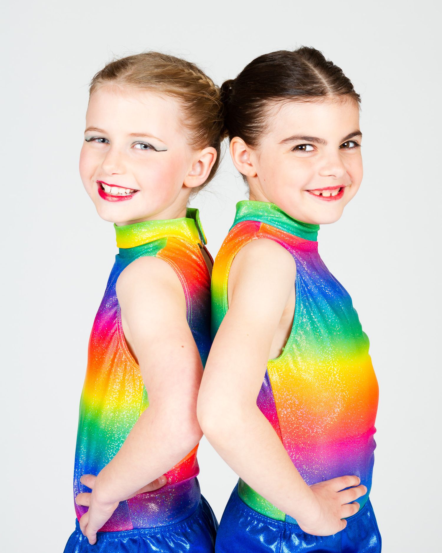 Two dancers in rainbow gradient leotards pose back to back against a white background.