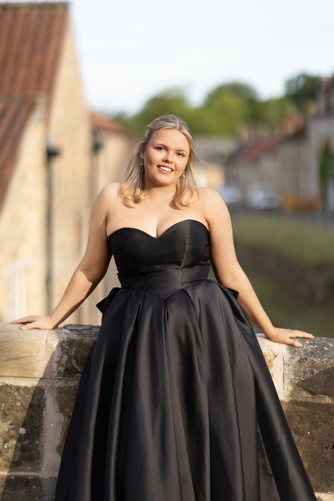 A classic black strapless ballgown photographed against stone walls outdoors.