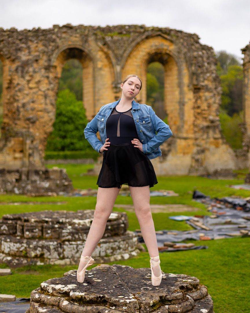 Dancer strikes dynamic poses among historic stone abbey ruins on green grass.