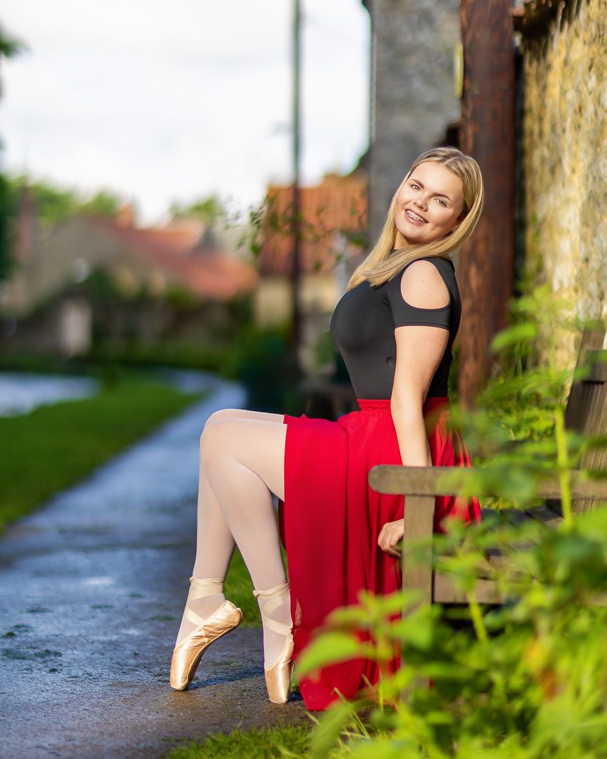 Ballet dancer in red dress performs elegant poses along a garden path.