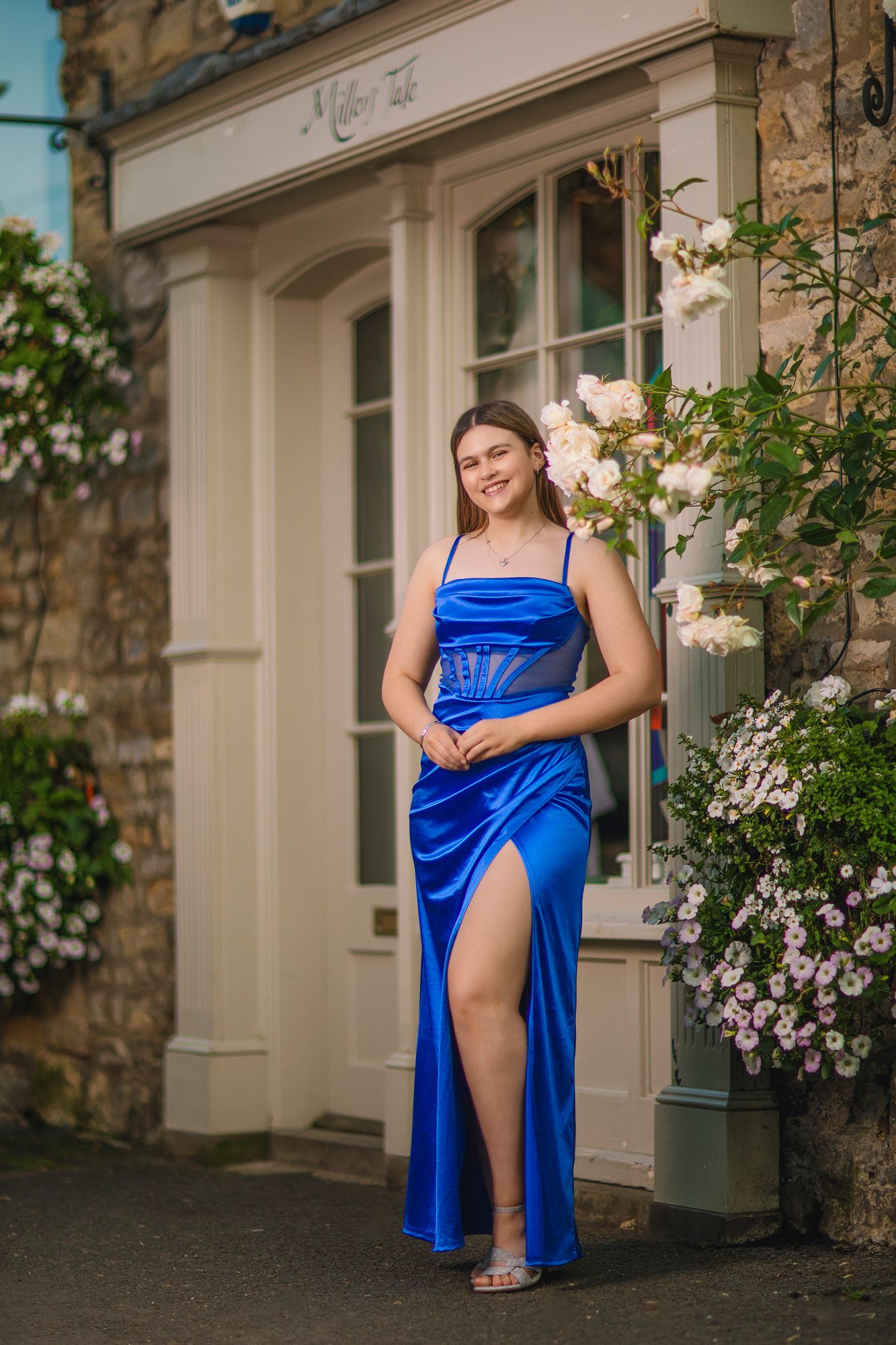 Royal blue evening dress captured against stone wall with climbing roses.
