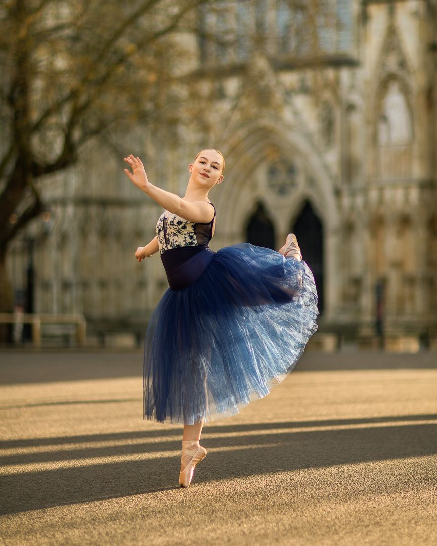 Dancer in blue tulle skirt performs graceful movements against historic architecture backdrop.