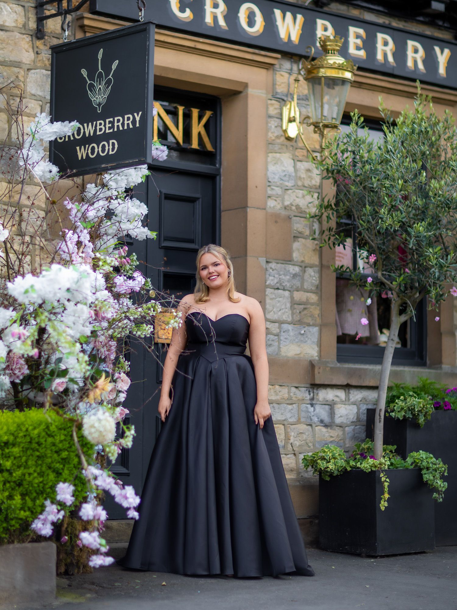 An elegant black gown poses outside the Crowberry establishment with floral decorations.