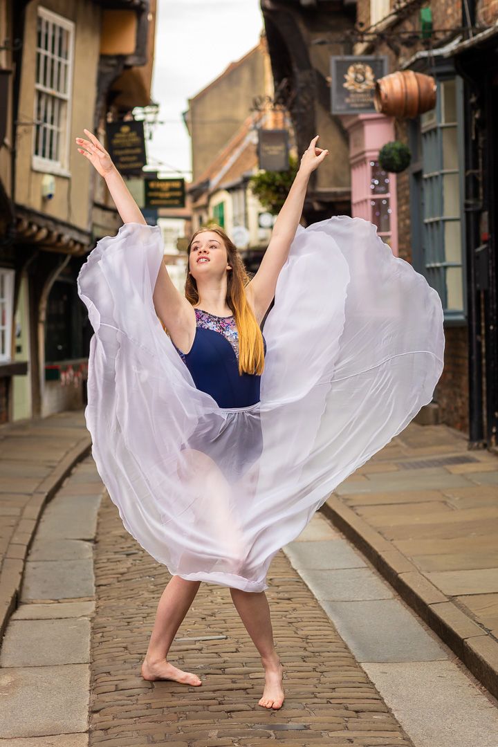 Dance performance photos on cobblestone street featuring flowing white dress movement.