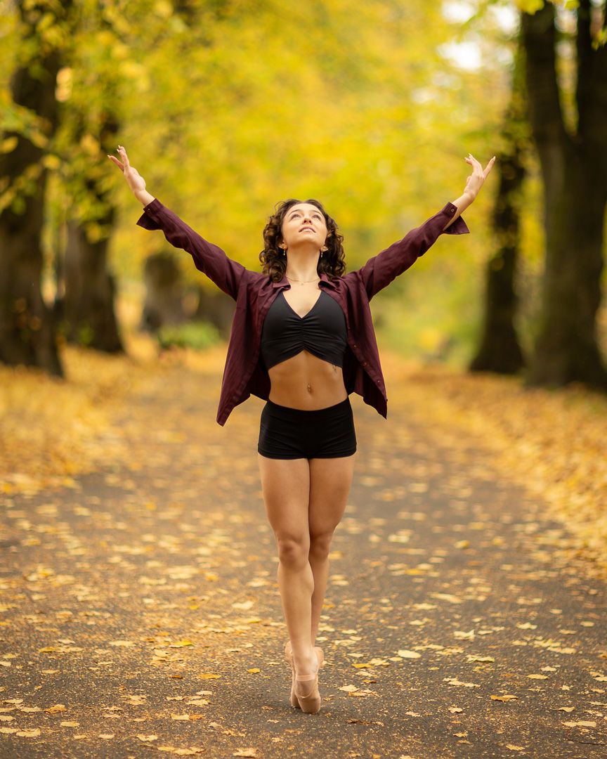 Expressive dance movements captured on autumn path covered in yellow leaves.