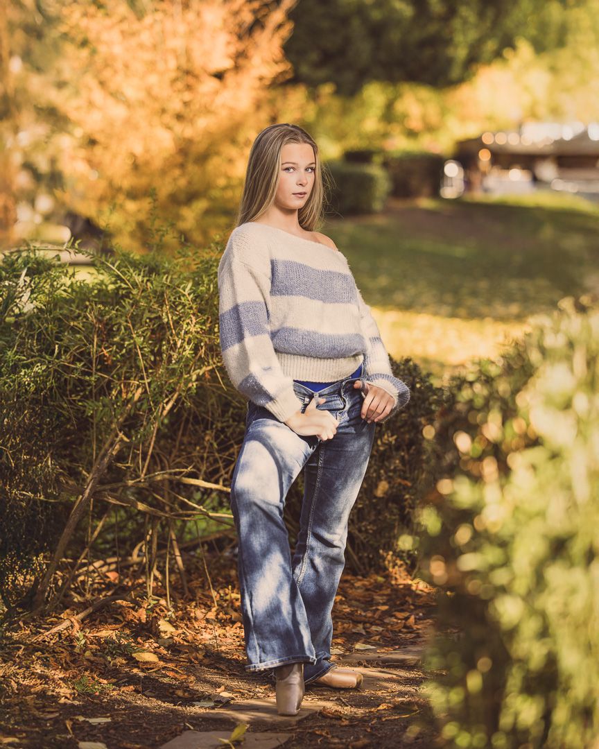 Casual fall fashion portrait featuring striped sweater and jeans amid autumn foliage.