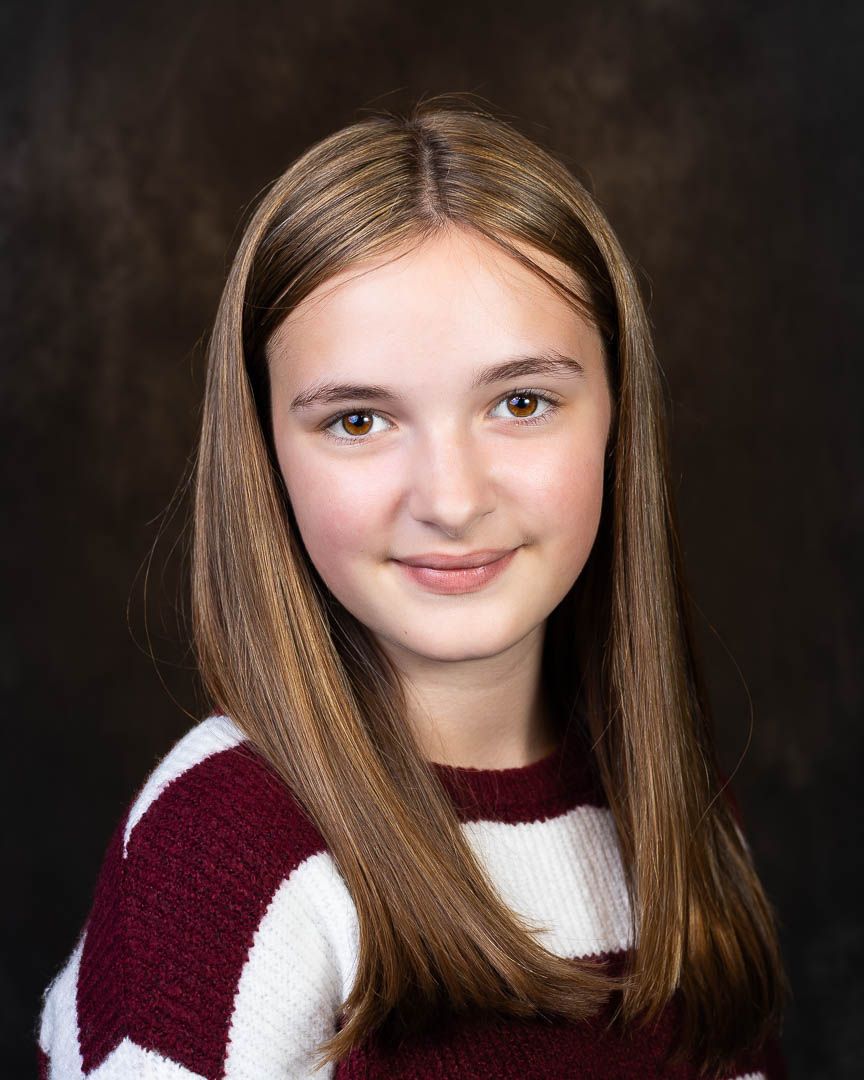 Young girl with long brown hair smiles warmly in a maroon and white striped sweater for a school portrait.
