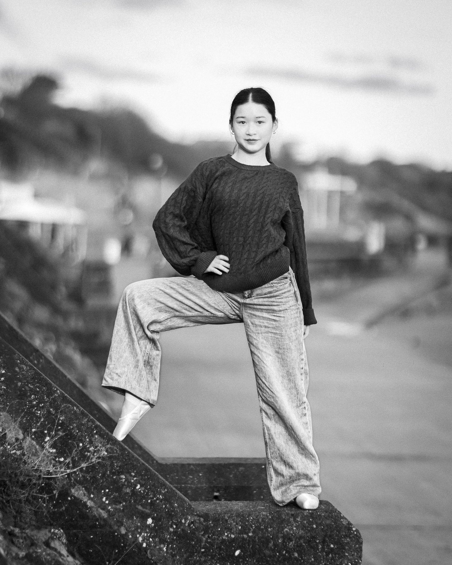 A person in dark clothing stands on a rocky hillside against a blurred background landscape.