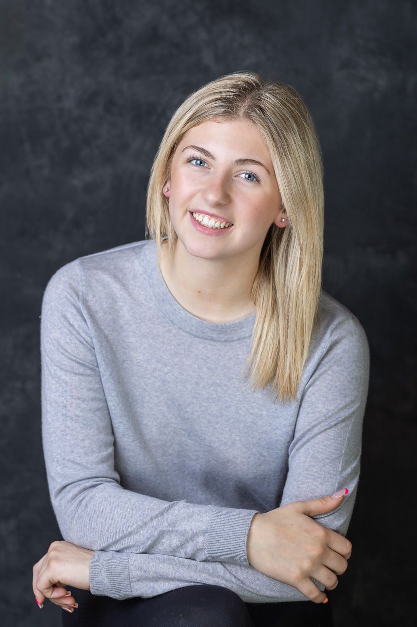 Studio portrait of person in grey sweater against dark background.