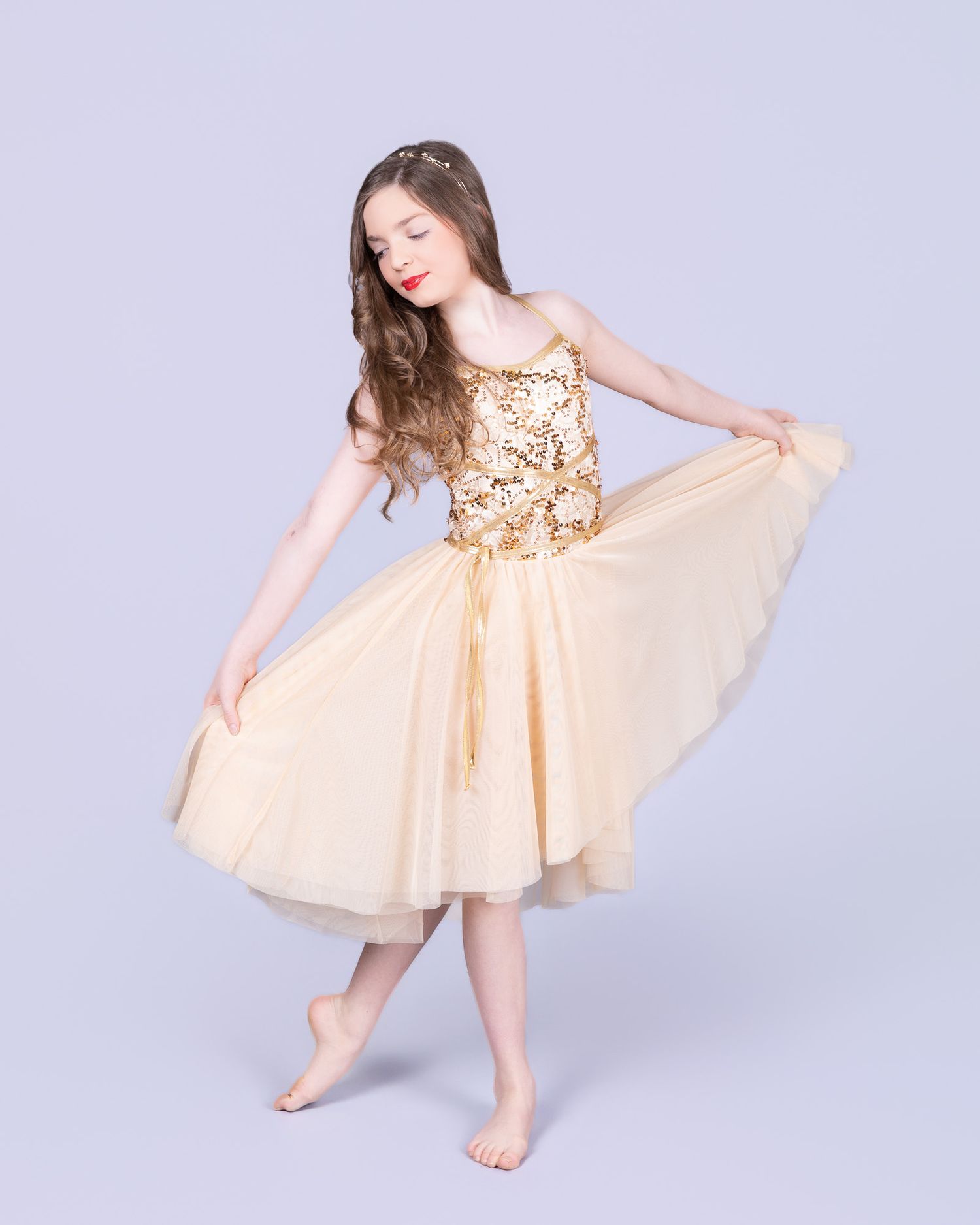 Young dancer in a peach-colored dress twirls gracefully on a light gray studio backdrop.