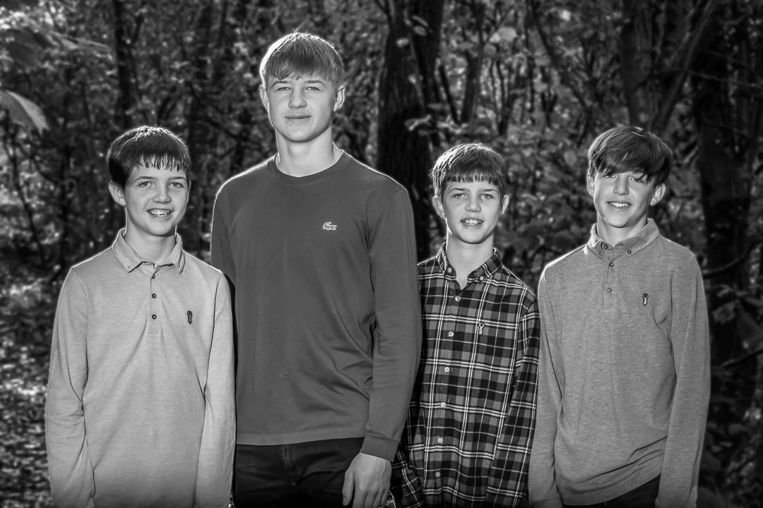 Group of young people standing together outdoors in casual clothing against a wooded background.