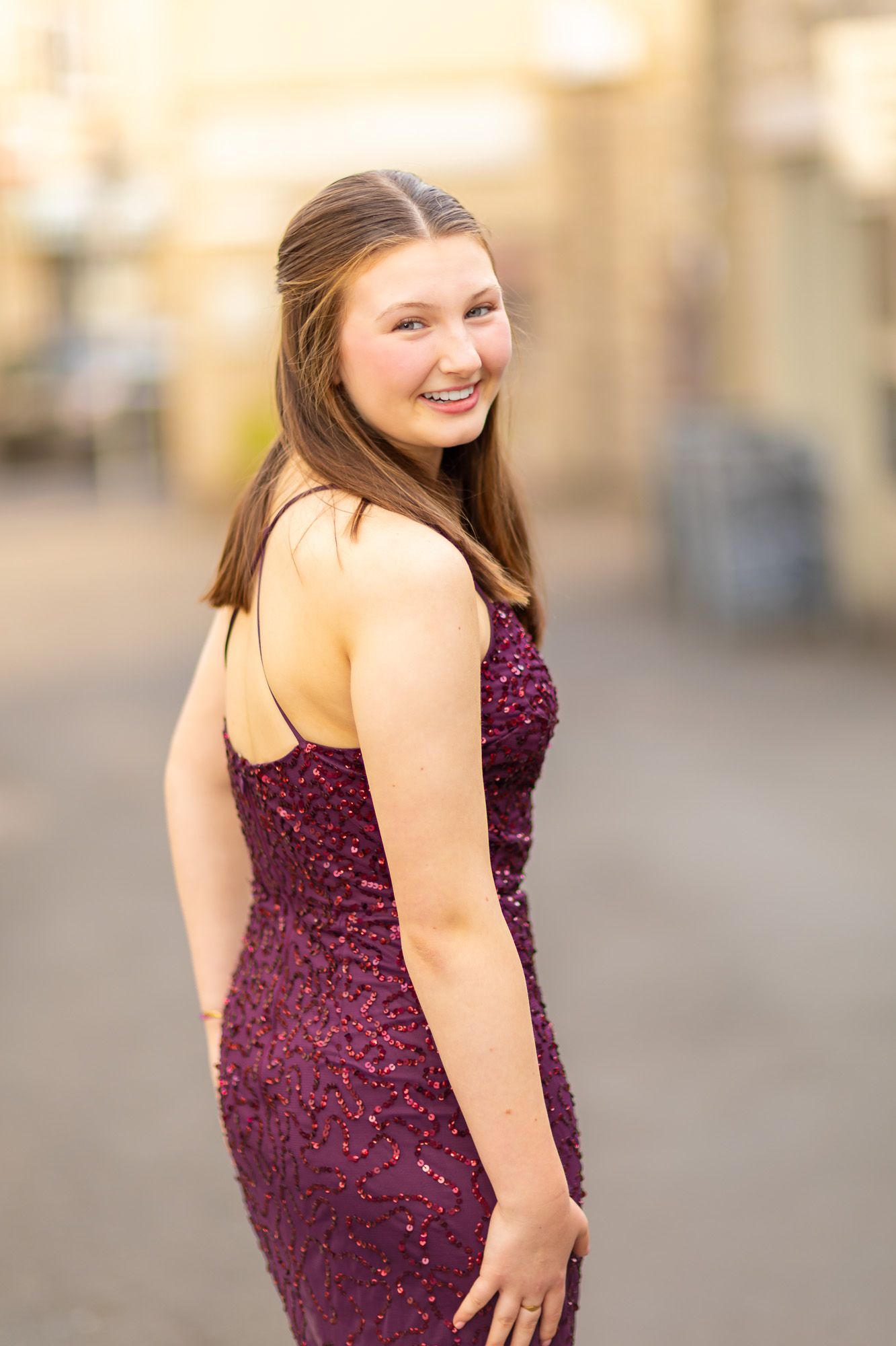 A person in a sparkly burgundy formal dress poses outdoors against a blurred background.