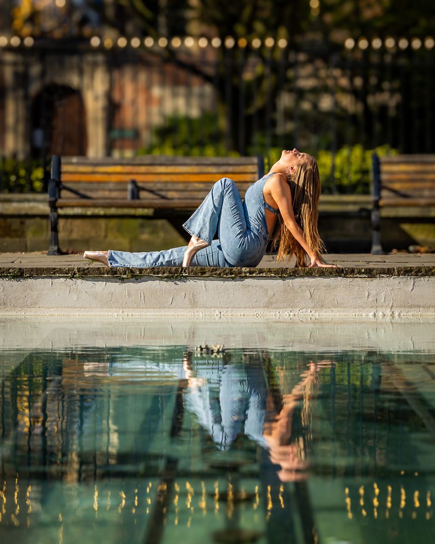Artistic portrait of dancer reclining by reflective pool with mirror image in water.