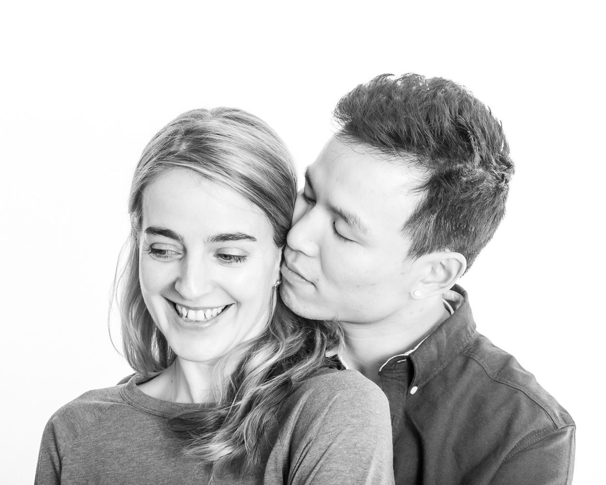 Black and white portrait of a couple sharing an intimate moment against white background.