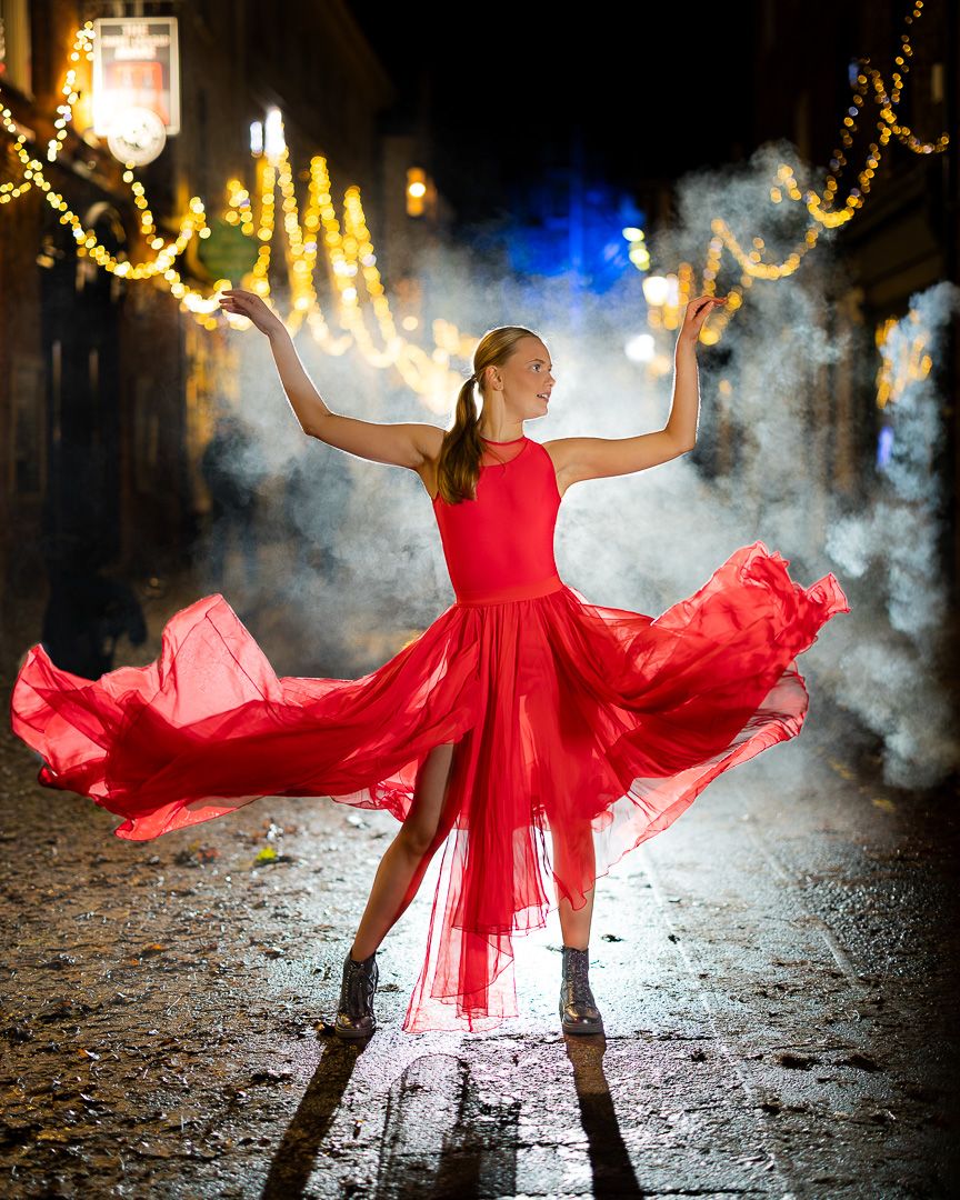 A flowing red dress twirls dramatically against a dark background with twinkling lights and atmospheric fog.